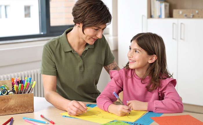 Therapeutin unterstützt ein Mädchen bei einer Schreib- und Lernübung am Tisch
